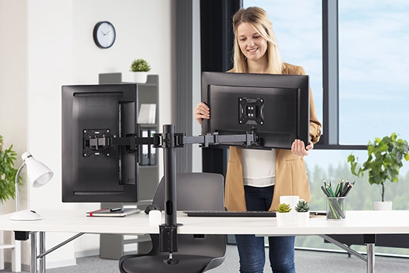 A young woman aligns her second monitor in her office using the Hama monitor mount